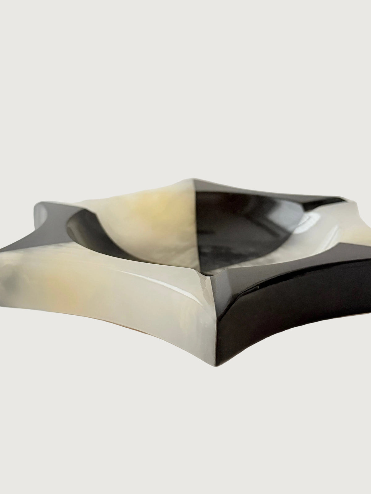 A geometric star-shaped onyx bowl with alternating black and  white marbled sections, photographed from the side on a plain off-white background. Home Decor. Vintage. Collectible. 