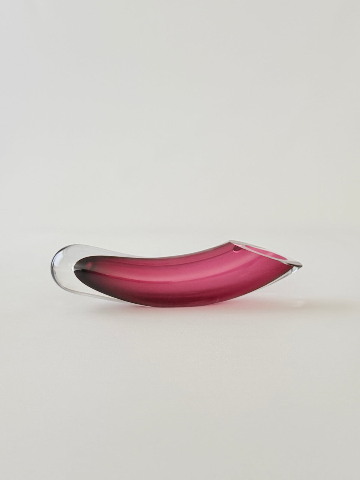 A cranberry and clear curved glass sommerso horizontal vase on a seamless light gray background.