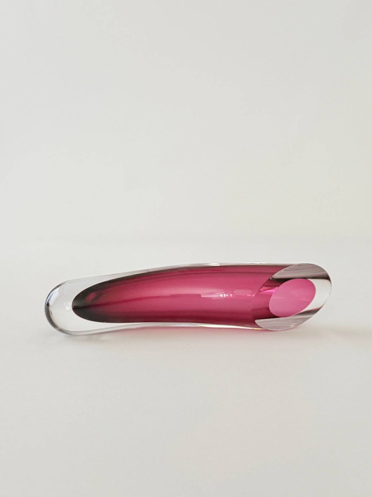 A cranberry and clear curved glass sommerso horizontal vase seen from top angle on a seamless light gray background.