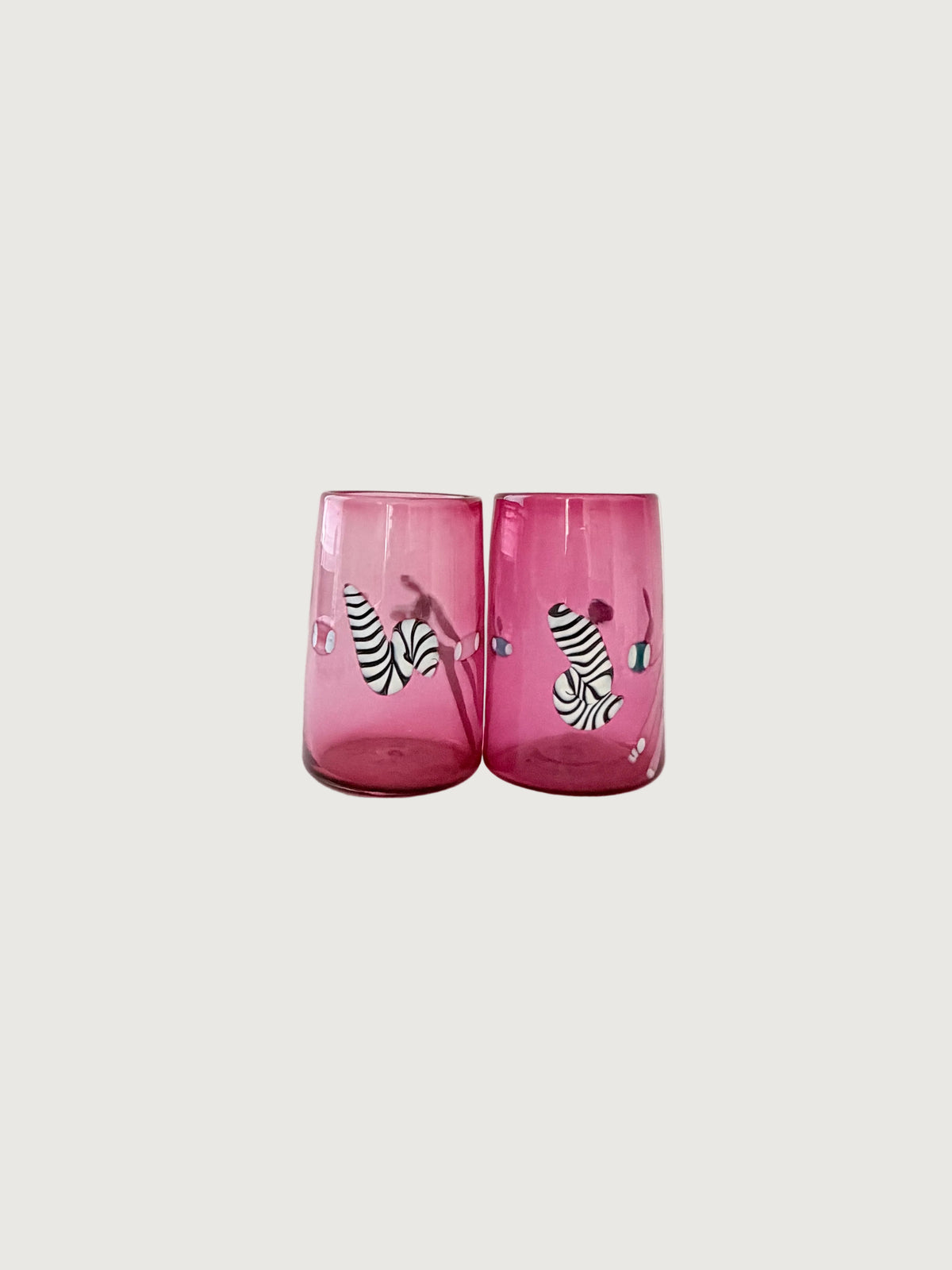 A pair of pink glass tumblers with black and white zebra print and small colorful decorative details against a light gray background.