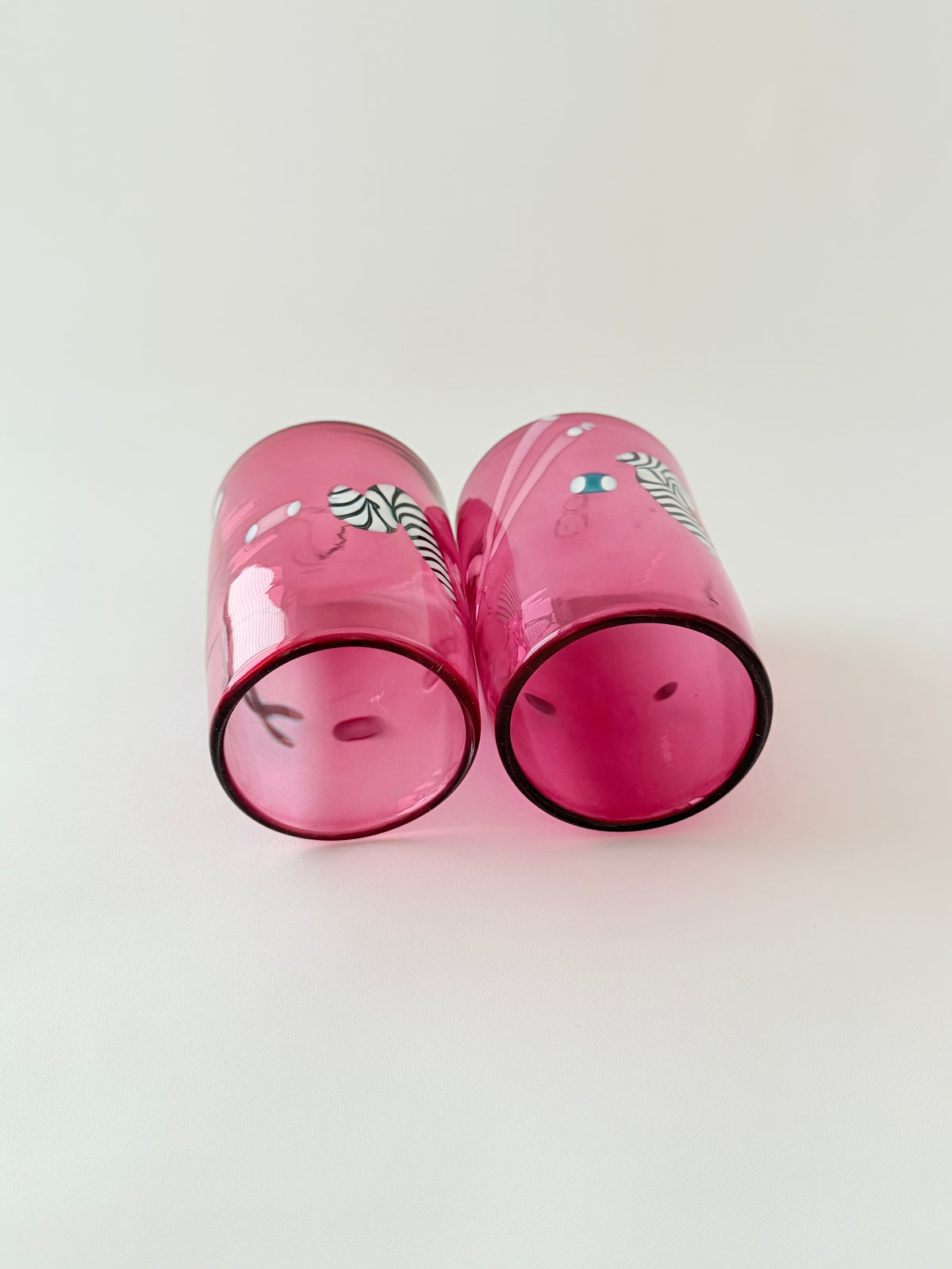 A pair of pink glass tumblers with black and white zebra print and small colorful decorative details on side to show inside on a light gray background.