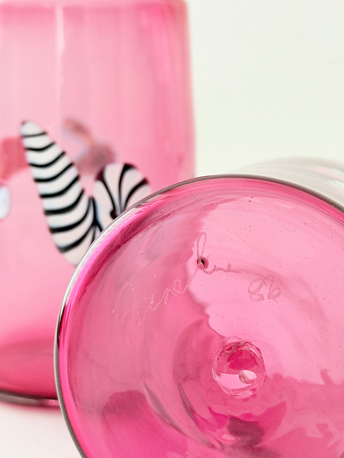 Closeup of the signature "Fineline" and the year '86 etched on a pink glass tumblers with black and white zebra print and small colorful decorative details.