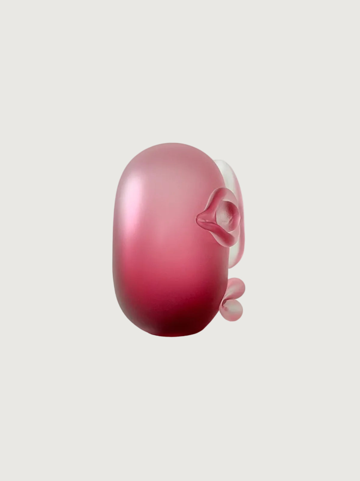A small sculptural object in pink glass with a rounded organic shape  photographed on a clean light gray studio background.
