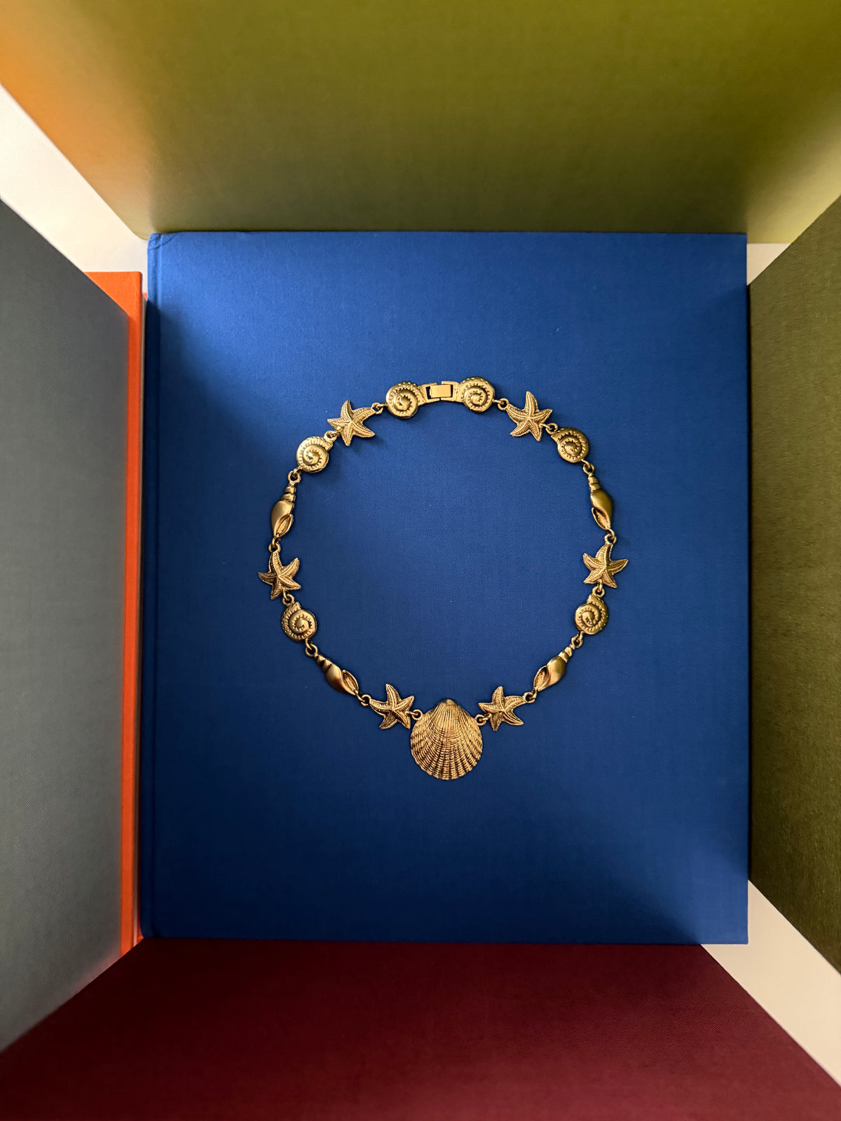 A gold-toned necklace featuring starfish and spiral shell motifs, displayed on a blue book