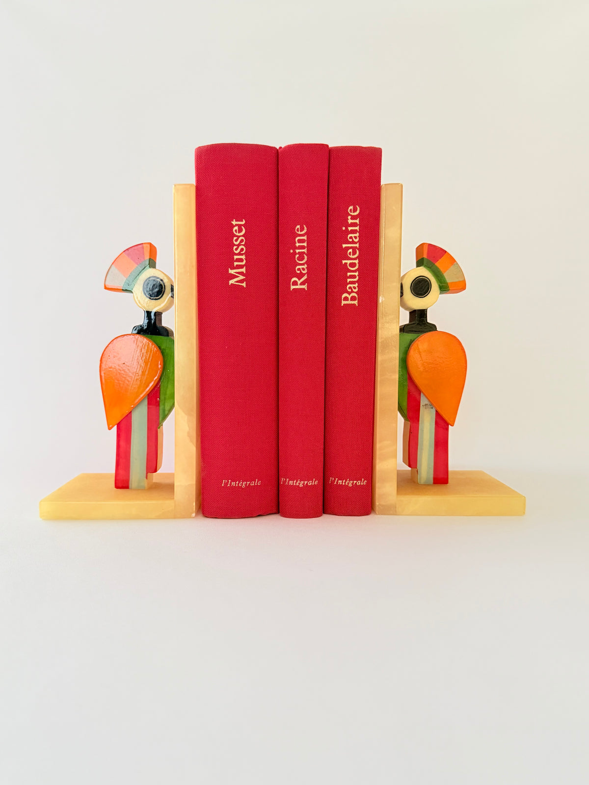 A pair of colorful alabaster bookends shaped like stylized birds holding books and set against a plain white background. Home Decor. Vintage. Collectible. 