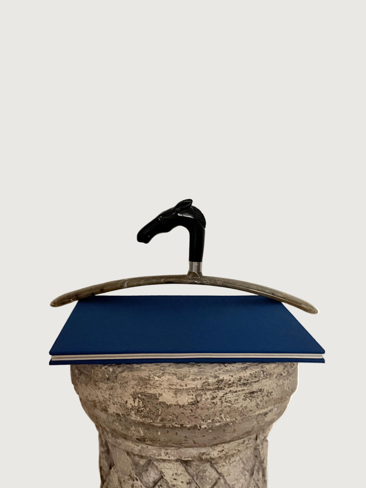Italian Black Horse Head  Hanger styled on top of a pedestal over a blue book