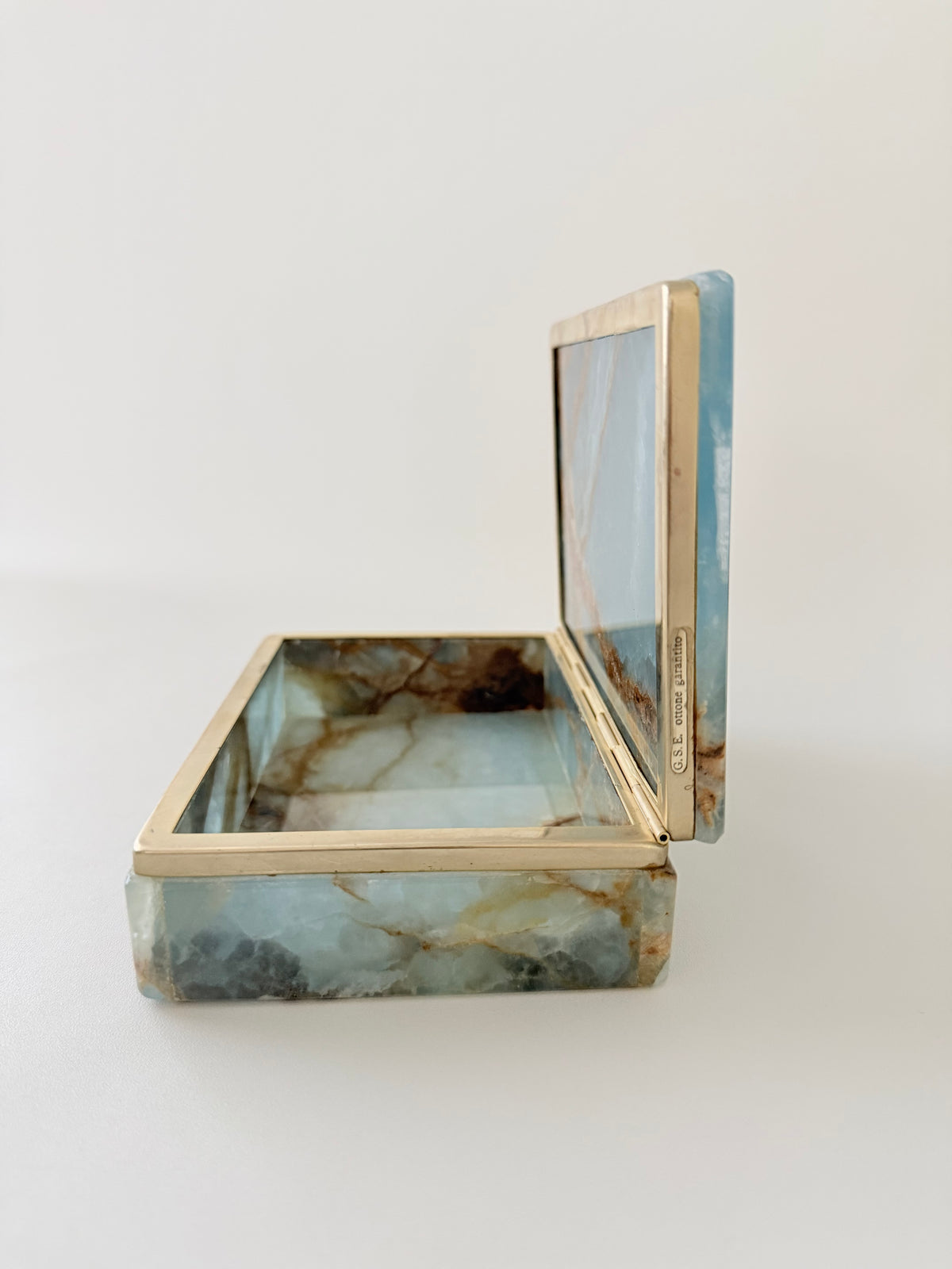 Side view of an open luxurious blue onyx vintage box with rust color veining and brass hinges. From Italy and made between 1950s and 1970s and comes with its original G.S.E. Ottone Garantito sticker. Home Decor. Vintage. Collectible. 