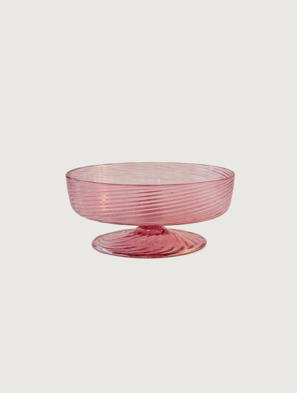 A pink glass pedestal bowl with a ribbed, spiral texture, set against a plain light beige background.