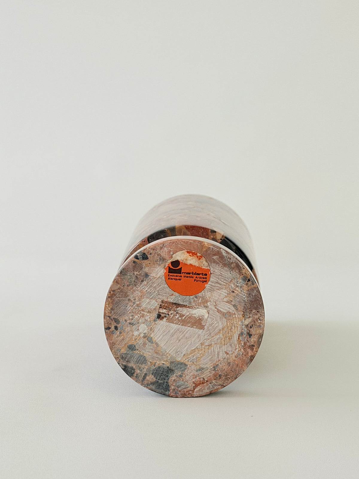 Sticker at the bottom of a breccia marble cylindrical vase  with a natural earth-toned stone featuring a fragmented, multicolored "brecciated" look and veining.