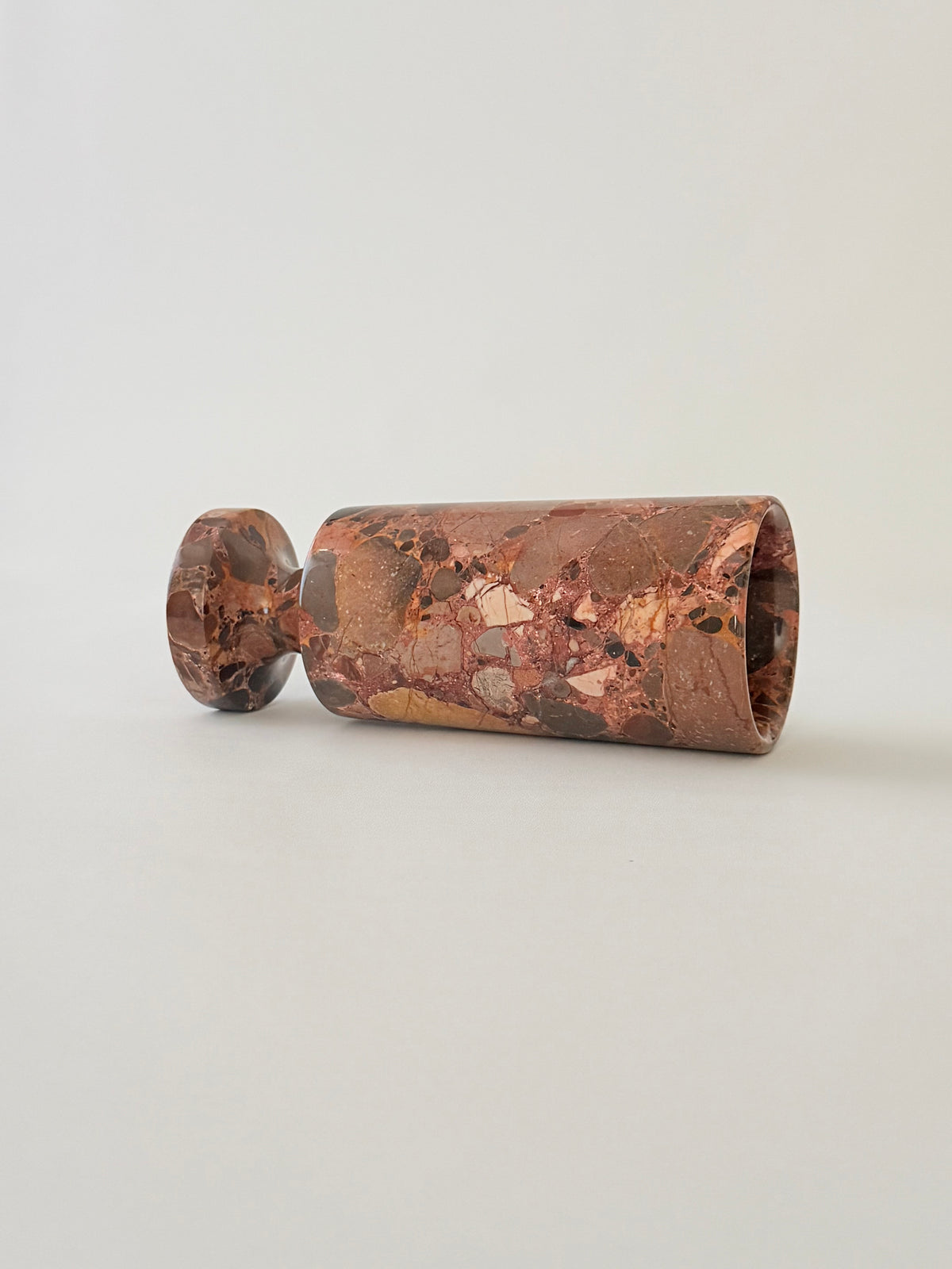 A breccia marble cylindrical vase  with a natural earth-toned stone featuring a fragmented, multicolored "brecciated" look and veining on its side.