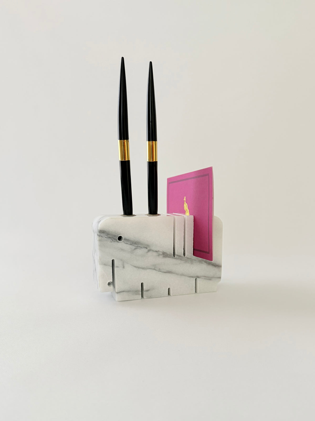 Two pens in a white and gray marble elephant penholder with slots for two pens and a note on a gray background.