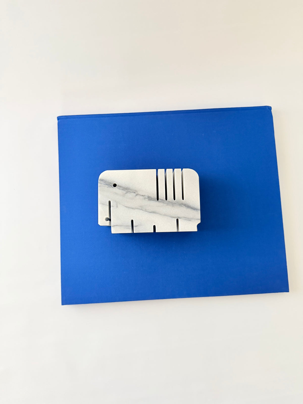 White and gray marble elephant penholder with slots for two pens and four slots lying on its side on a blue book