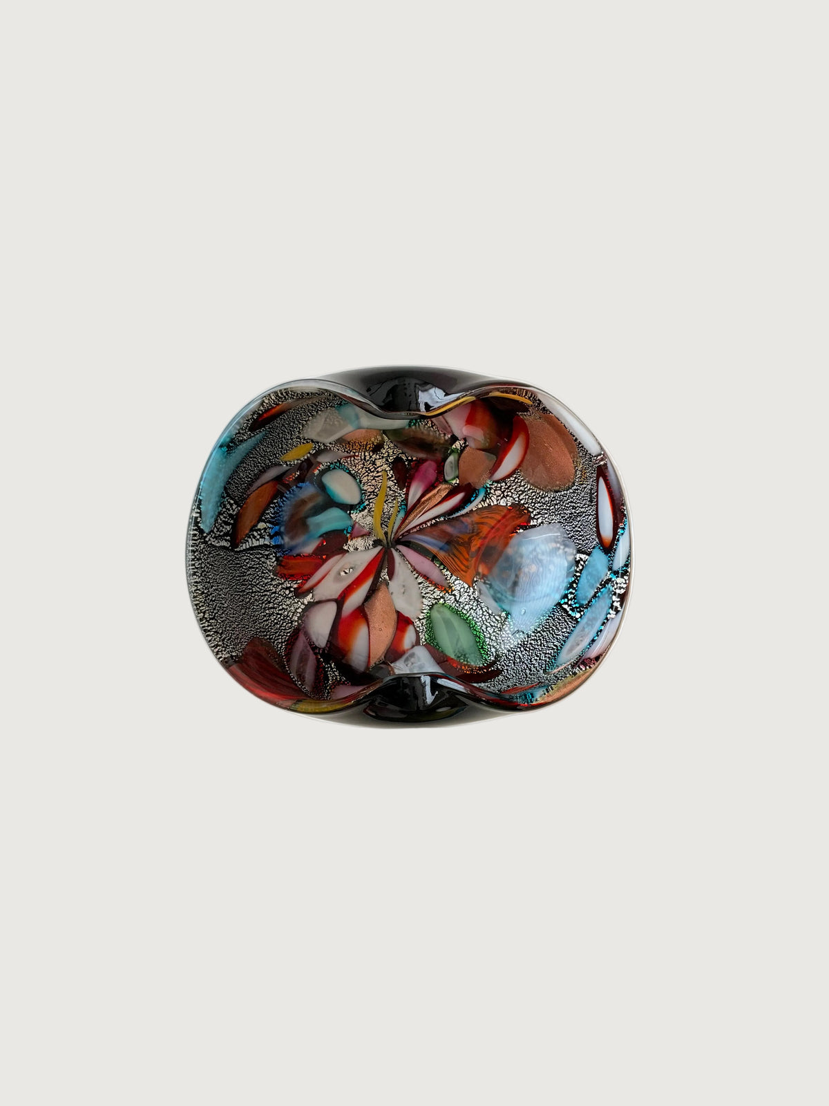 A striking mid-century hand-formed Murano "Tutti Frutti" bowl with two soft folds on thick black glass, a form used for bowls and ashtrays. Inside are bold colored fragments, cane sections on silver leaf and aventurine, copper crystals that make the glass sparkle.
