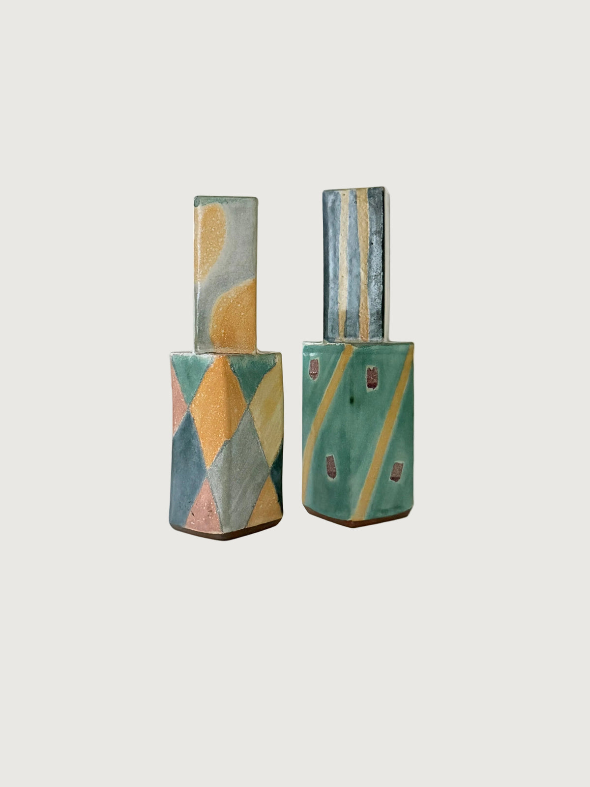Two ceramic candleholders decorated with abstract geometric patterns in teal, mustard yellow, and soft blue, set against a plain light background.