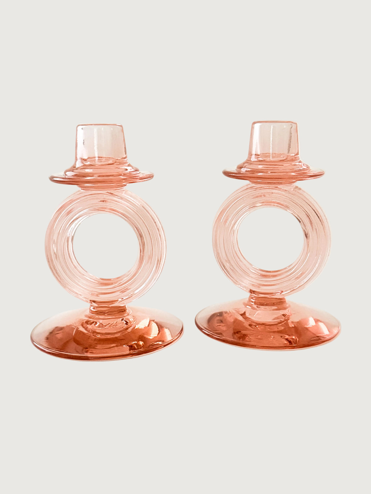 A pair of translucent peach-pink glass candle holders with a circular ring design and a small top cup, shown on a light gray background.