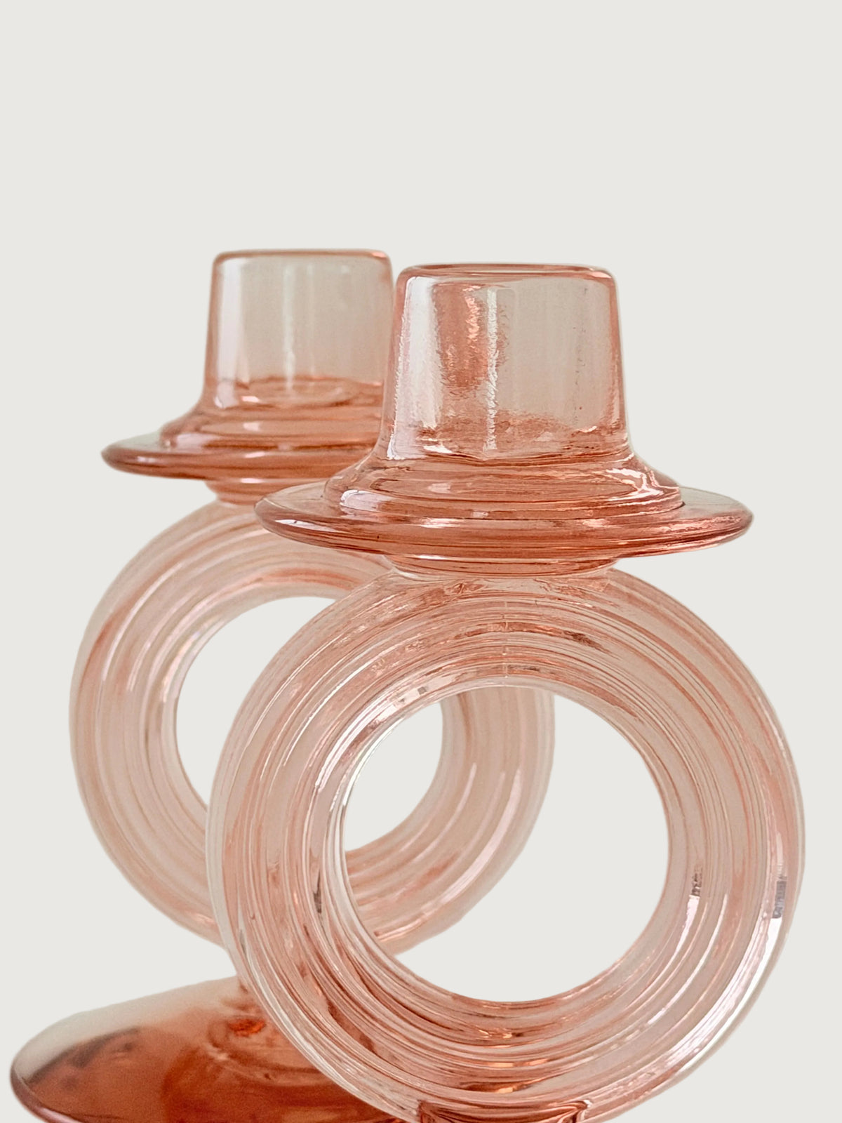 Two translucent pink glass candle holders with concentric circular rings and flared tops, photographed against a soft light beige background.