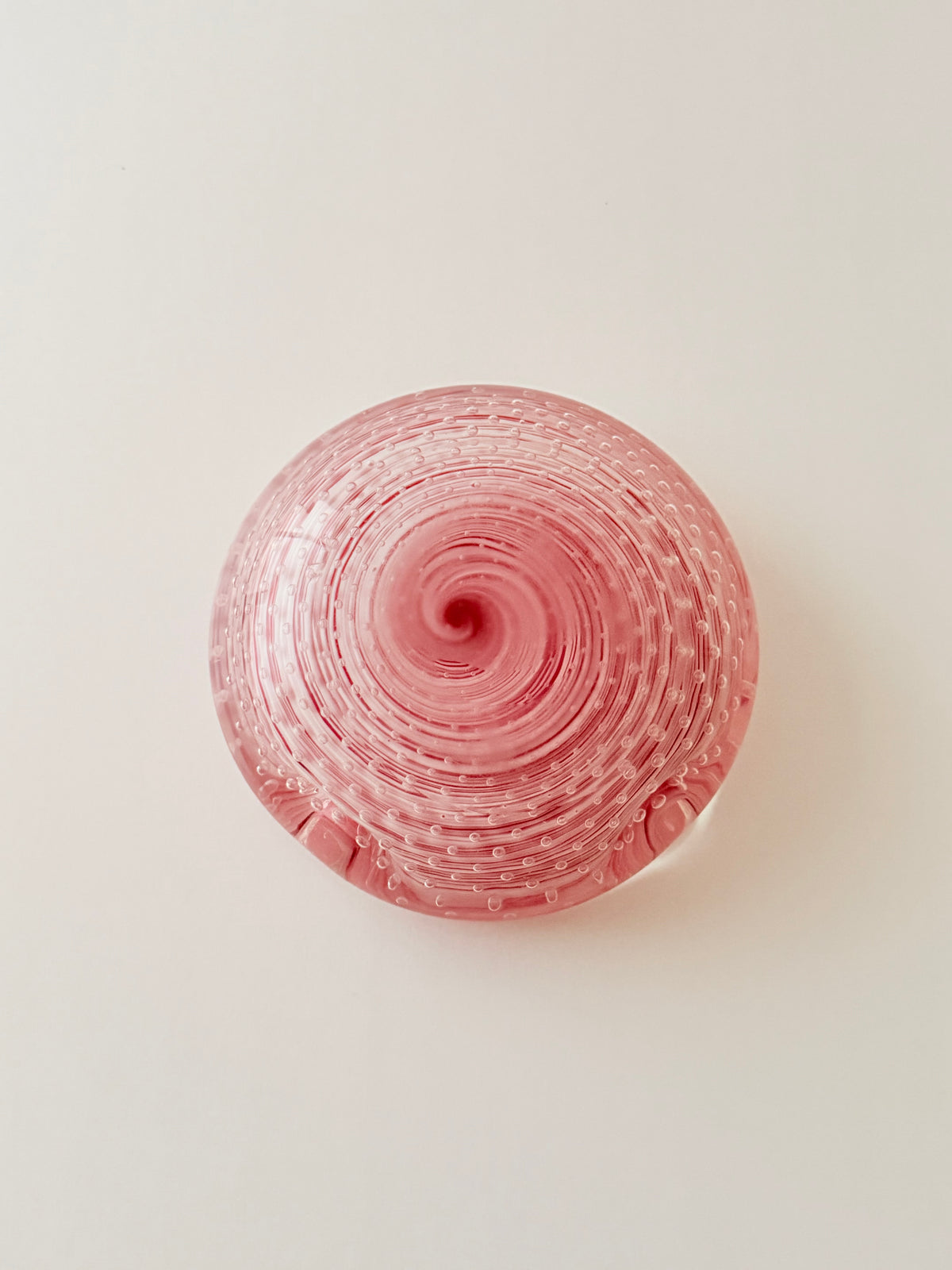 The back of a  round vibrant pink glass ashtray with a textured, bubble-filled design, set against a plain light gray background.Home Decor. Vintage. Collectible. 