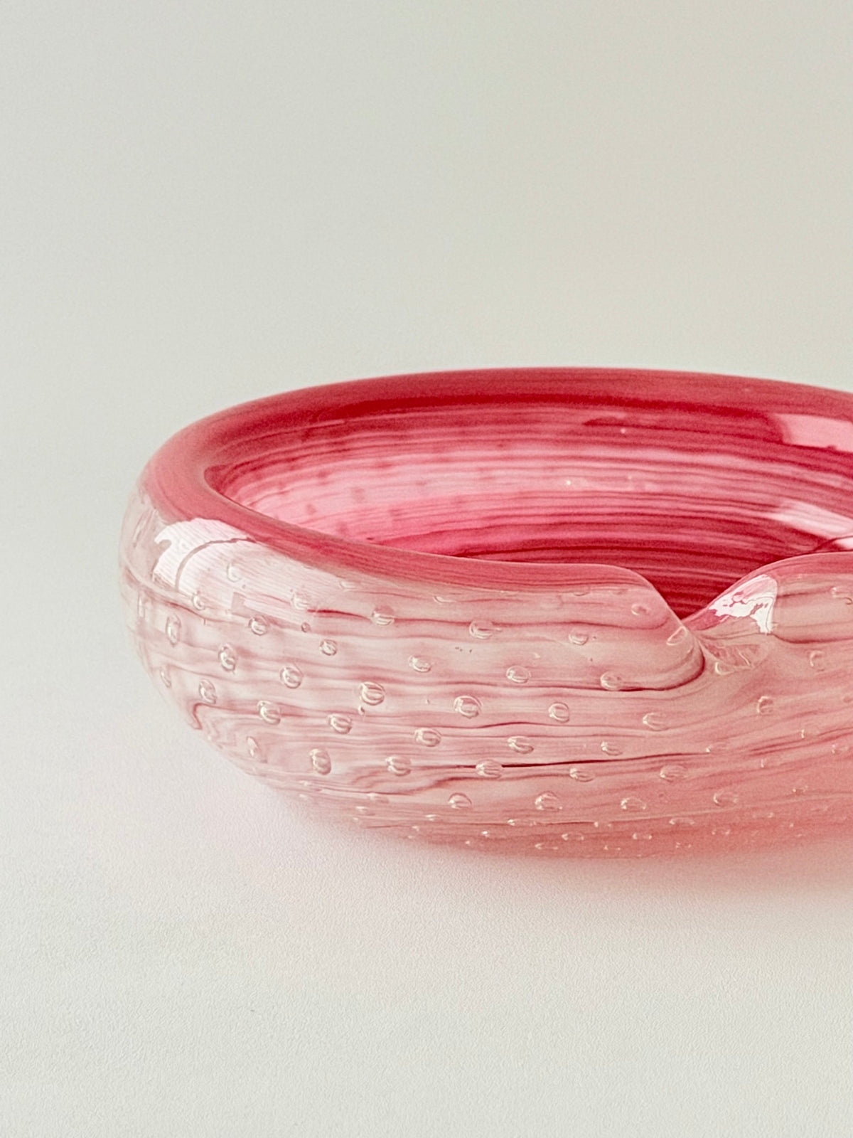Detail shot of a round vibrant pink glass ashtray with a textured, bubble-filled design, set against a plain light gray background.Home Decor. Vintage. Collectible. 
