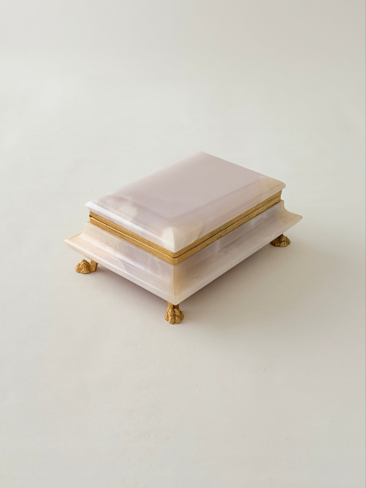 A rectangular pale pink onyx box accented by a gold metal trim and four claw feet, photographed on a clean off-white background.