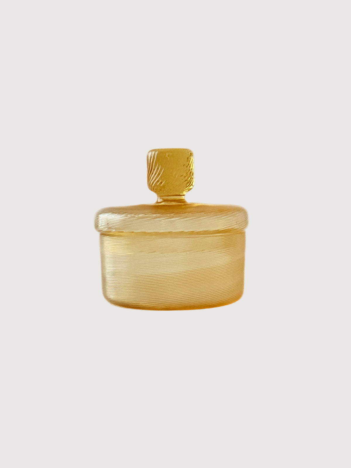 A small amber glass jar with a matching lid and a textured cylindrical handle, set against a plain off-white background.