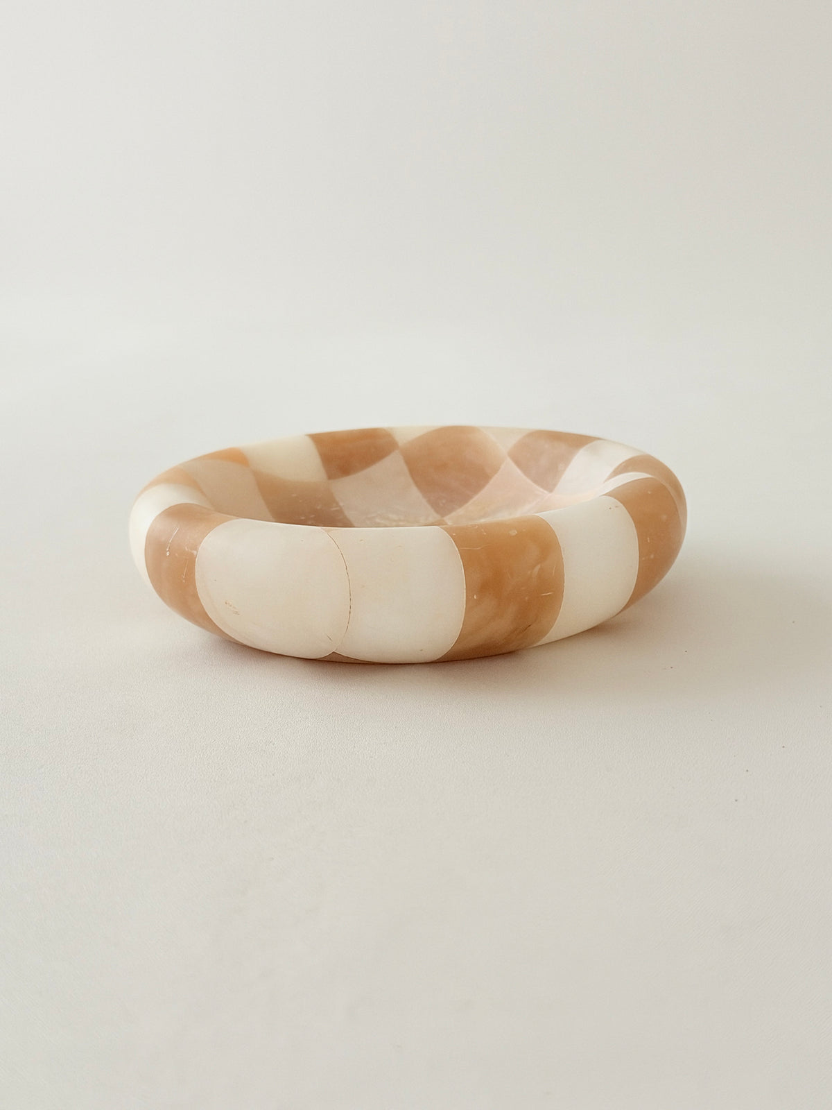 A  round alabaster bowl with a checkered pattern of warm tan and off-white, 