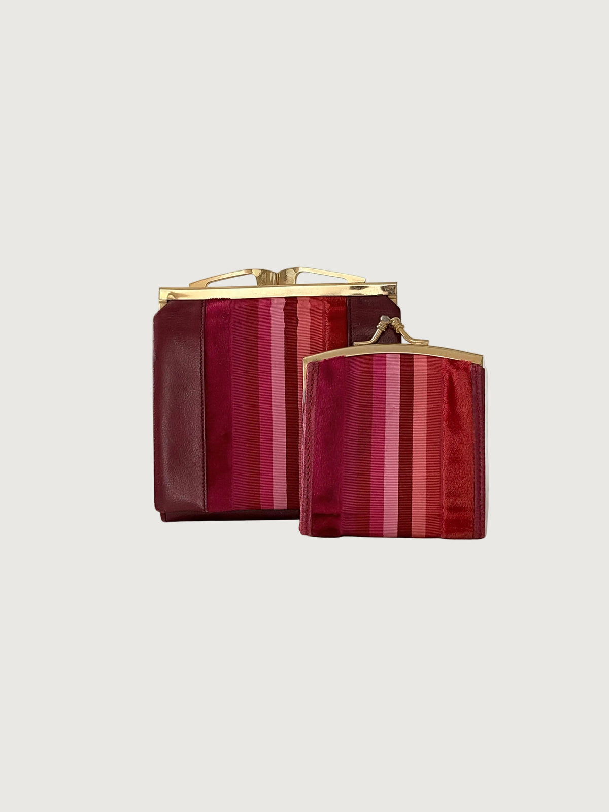 Two wallets with vertical pink and red stripes, gold-tone metal frames, and top clasps, photographed on a clean light gray studio background.