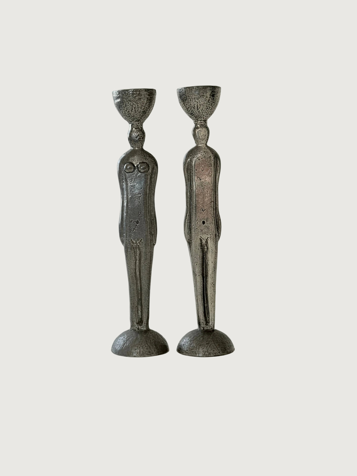 A pair of sculptural pewter candleholders shaped like stylized human figures, standing side-by-side against a plain, light gray background. Home Decor. Vintage. Collectible. 